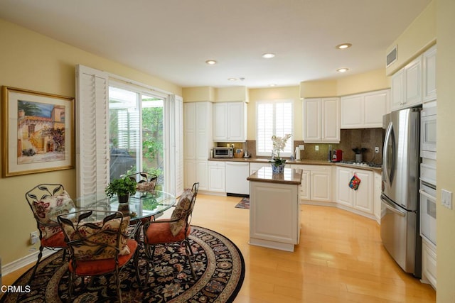 kitchen with white cabinets, light wood finished floors, appliances with stainless steel finishes, a center island, and tasteful backsplash