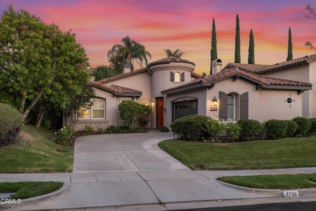 mediterranean / spanish house featuring stucco siding, a garage, driveway, a tiled roof, and a front lawn