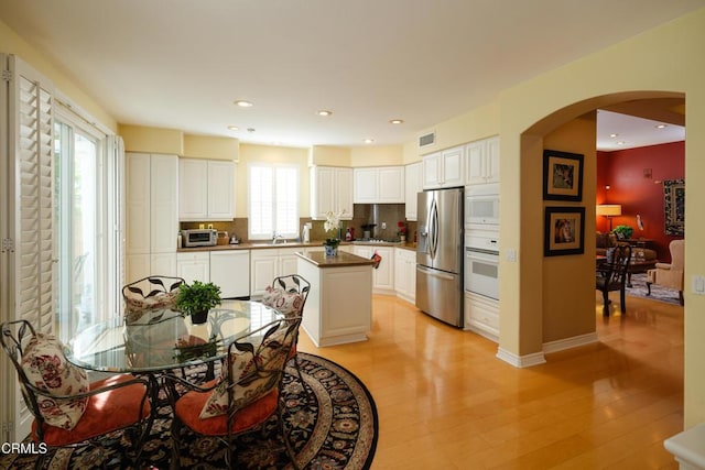 kitchen featuring light wood-style floors, arched walkways, white appliances, and backsplash