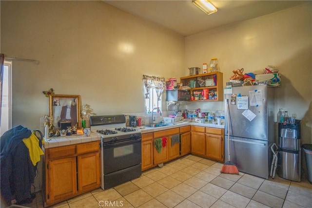 kitchen featuring range with gas cooktop, tile countertops, freestanding refrigerator, a sink, and light tile patterned flooring