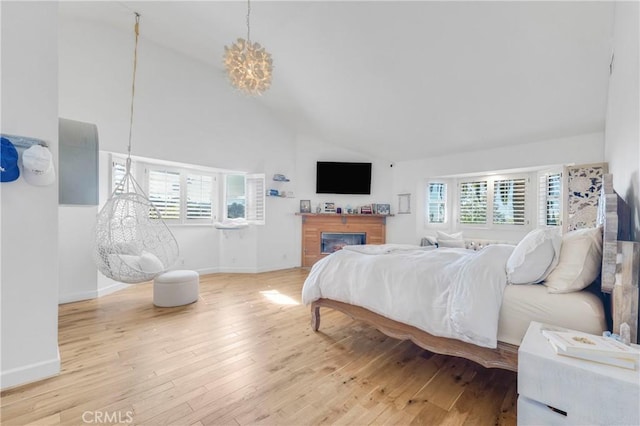 bedroom with baseboards, high vaulted ceiling, wood finished floors, and a glass covered fireplace
