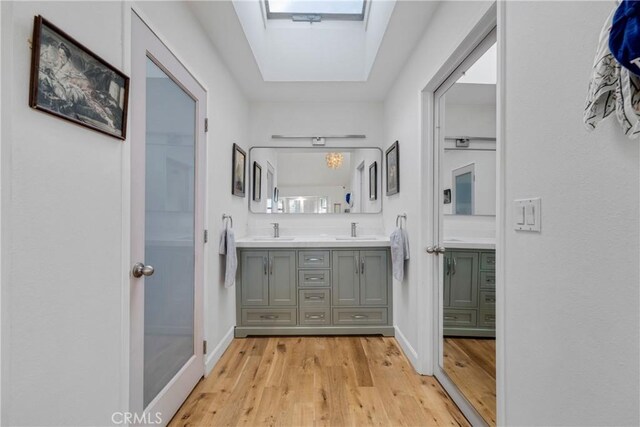 full bath featuring double vanity, a skylight, a sink, and wood finished floors