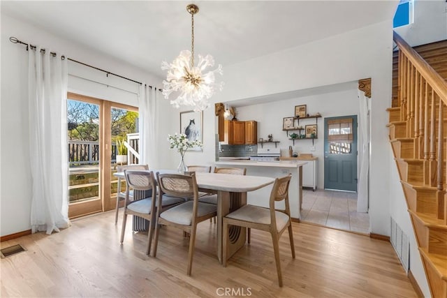 dining space featuring visible vents, baseboards, stairs, light wood-type flooring, and an inviting chandelier