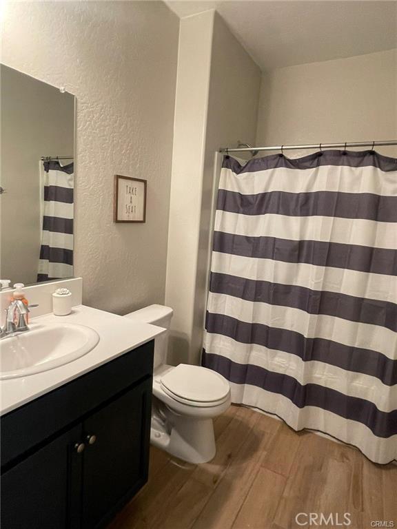 full bathroom featuring a textured wall, a shower with shower curtain, toilet, vanity, and wood finished floors