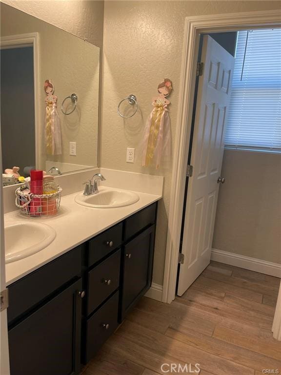 full bathroom with double vanity, a textured wall, a sink, and wood finished floors