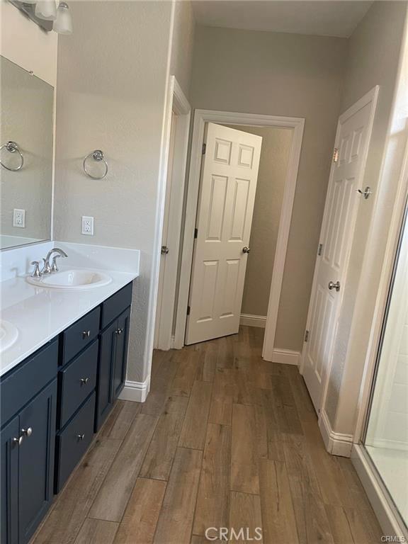 full bathroom with double vanity, a sink, baseboards, and wood finished floors