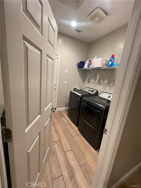 clothes washing area with laundry area, visible vents, baseboards, wood finish floors, and washing machine and dryer