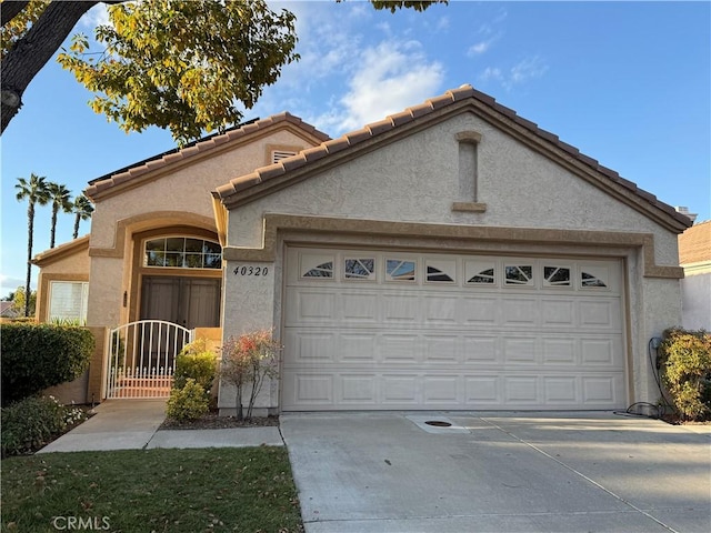 mediterranean / spanish-style home with concrete driveway, an attached garage, a gate, and stucco siding