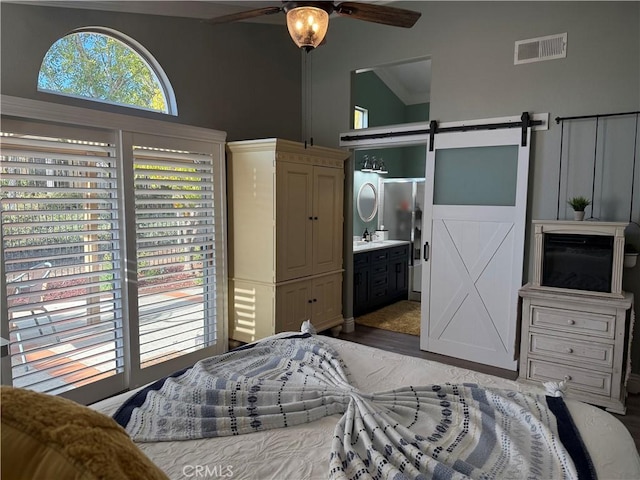 bedroom with a barn door, connected bathroom, wood finished floors, a sink, and visible vents