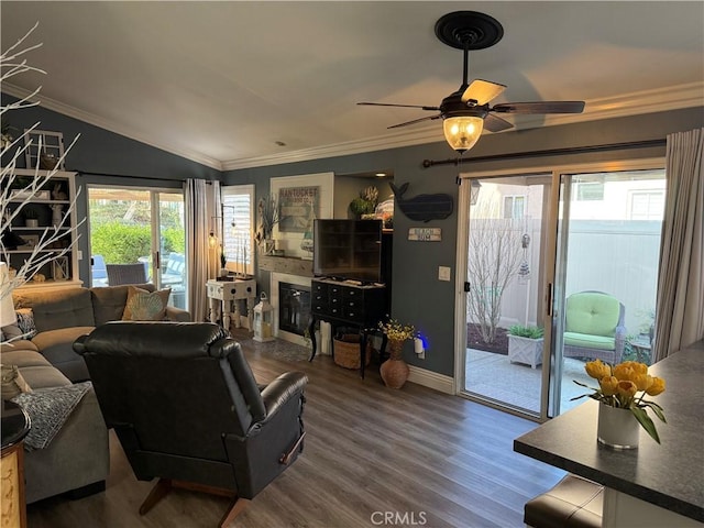 living room featuring baseboards, a glass covered fireplace, wood finished floors, vaulted ceiling, and crown molding