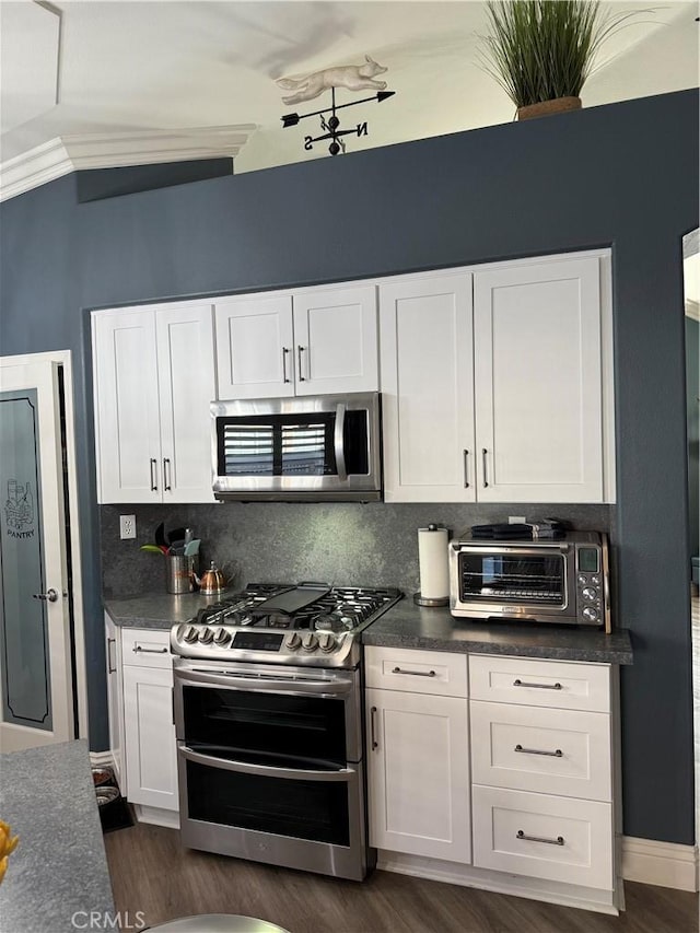 kitchen featuring a toaster, dark countertops, appliances with stainless steel finishes, white cabinetry, and backsplash