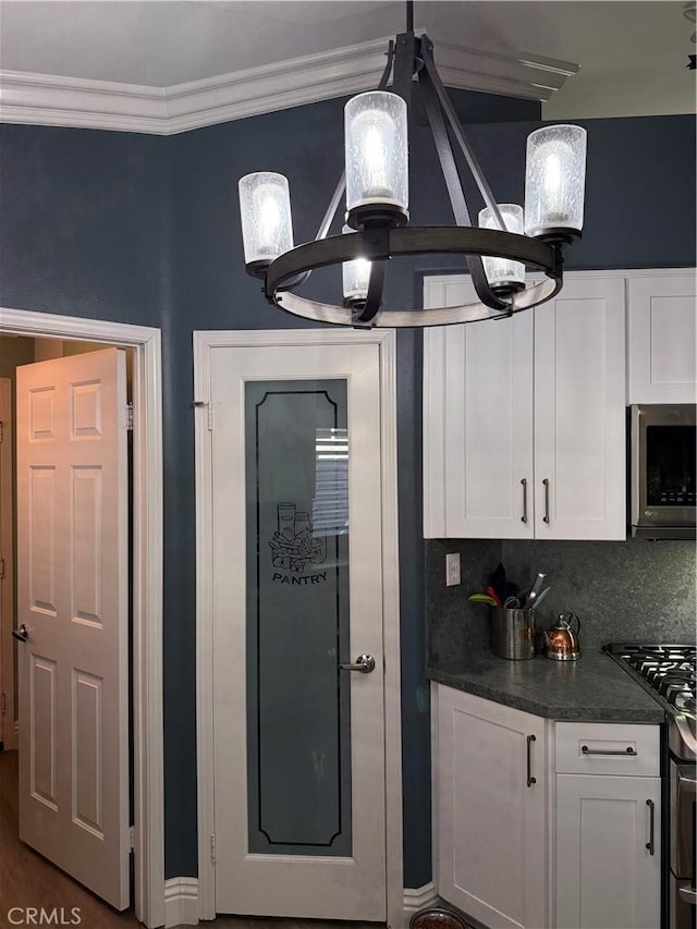 kitchen featuring white cabinets, appliances with stainless steel finishes, backsplash, dark countertops, and crown molding