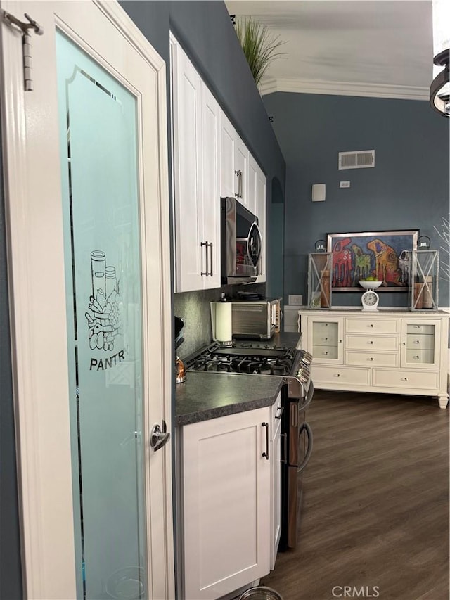 kitchen with stainless steel appliances, dark wood-style flooring, white cabinets, dark countertops, and crown molding