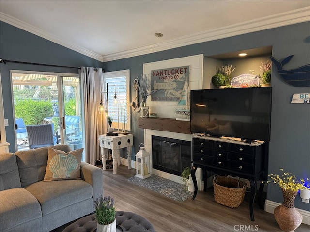 living room featuring lofted ceiling, wood finished floors, a fireplace with flush hearth, baseboards, and ornamental molding