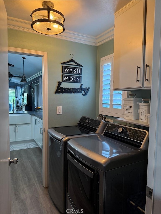 laundry room featuring wood finished floors, ornamental molding, washing machine and clothes dryer, and cabinet space