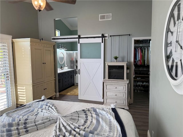 bedroom featuring visible vents, a closet, a barn door, wood finished floors, and high vaulted ceiling
