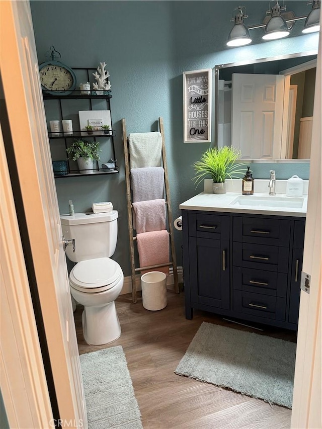 bathroom with toilet, baseboards, wood finished floors, and vanity