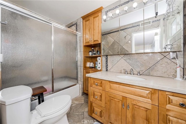 full bath with tasteful backsplash, vanity, toilet, and bath / shower combo with glass door