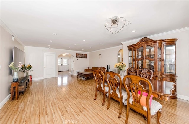 dining space with ornamental molding, arched walkways, light wood-style flooring, and baseboards