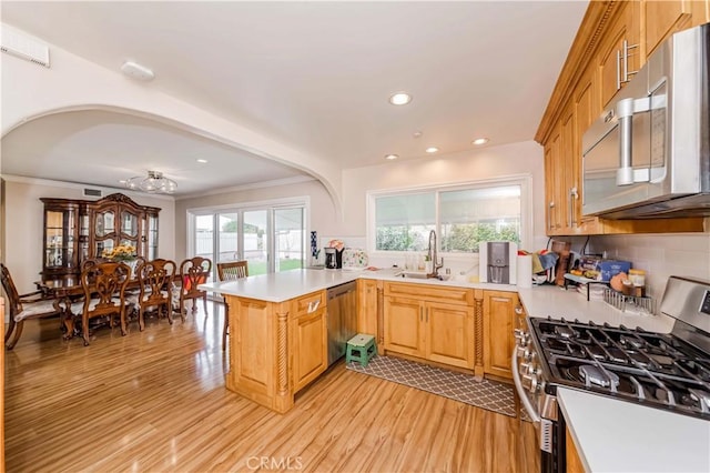 kitchen featuring light wood-style flooring, a peninsula, a sink, light countertops, and appliances with stainless steel finishes