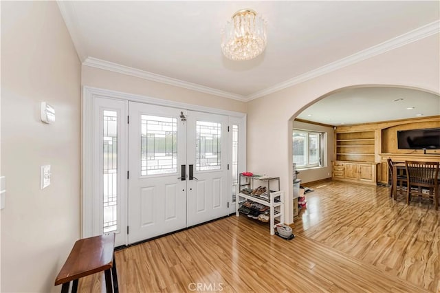 entrance foyer featuring a notable chandelier, crown molding, arched walkways, and wood finished floors