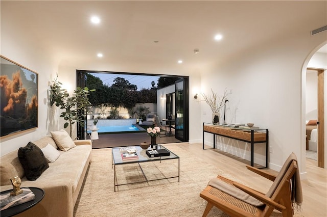 living area with arched walkways, wood finished floors, visible vents, and recessed lighting