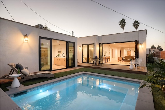 rear view of property with an outdoor pool and stucco siding