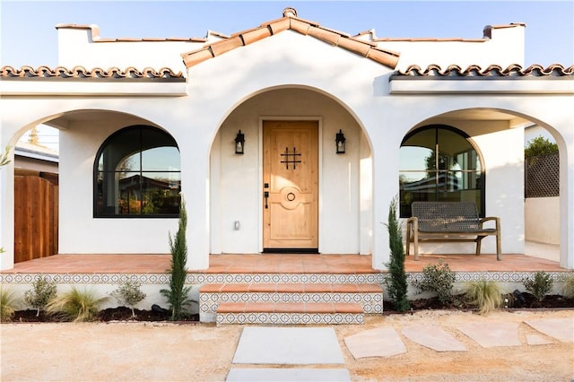 entrance to property featuring a tiled roof, covered porch, and stucco siding