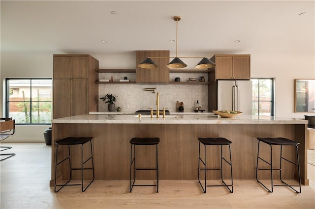 kitchen featuring high end refrigerator, a sink, light wood-type flooring, open shelves, and tasteful backsplash