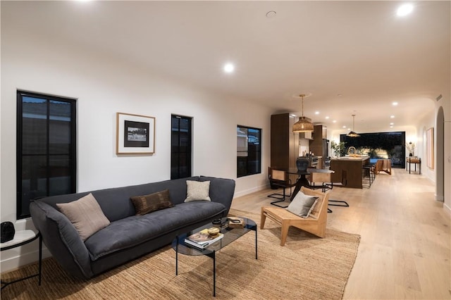 living area featuring light wood-style flooring, arched walkways, baseboards, and recessed lighting