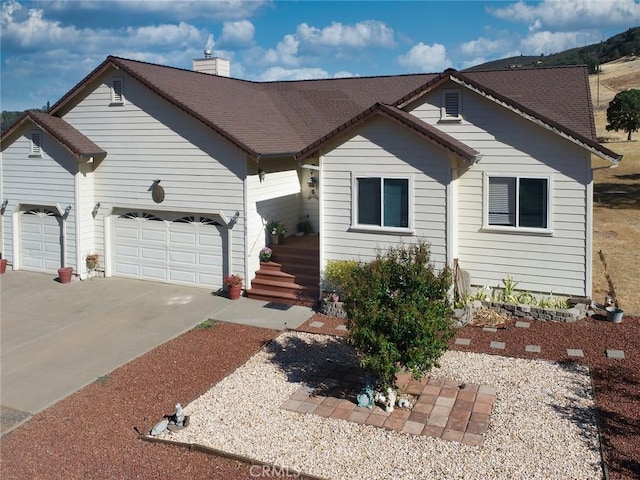 view of front of home with a chimney, concrete driveway, and an attached garage