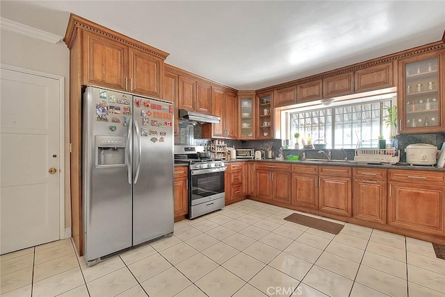 kitchen with tasteful backsplash, appliances with stainless steel finishes, brown cabinets, and under cabinet range hood