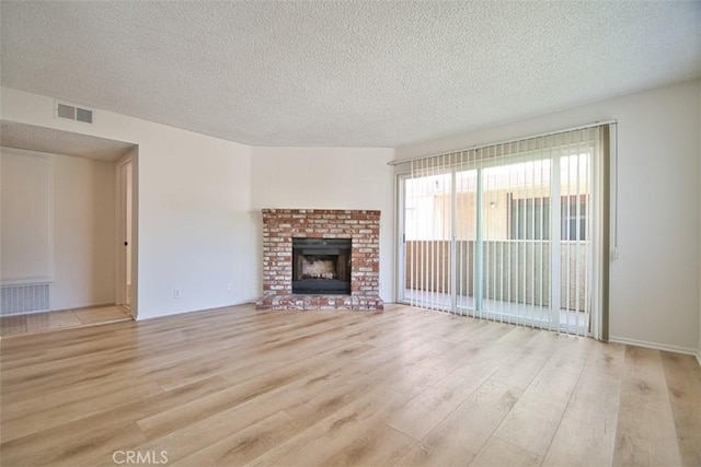 unfurnished living room featuring a textured ceiling, light wood finished floors, a brick fireplace, and visible vents