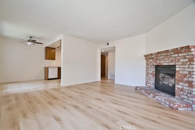 unfurnished living room with a brick fireplace, a ceiling fan, light wood finished floors, and a textured ceiling