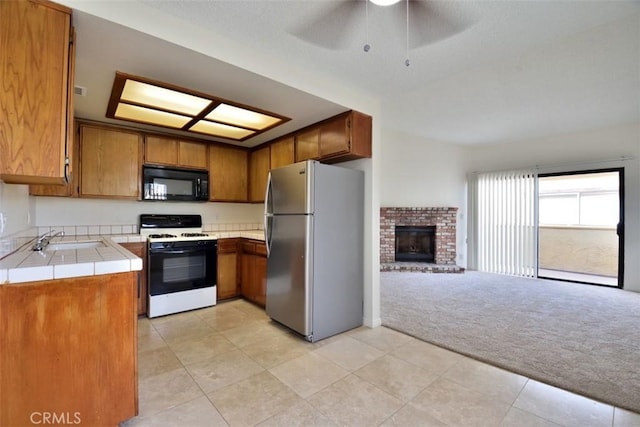 kitchen featuring light colored carpet, tile countertops, freestanding refrigerator, black microwave, and gas stove