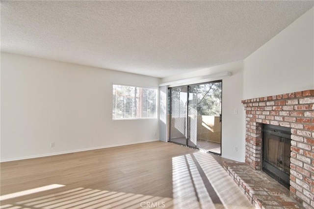 unfurnished living room featuring a brick fireplace, a textured ceiling, baseboards, and wood finished floors