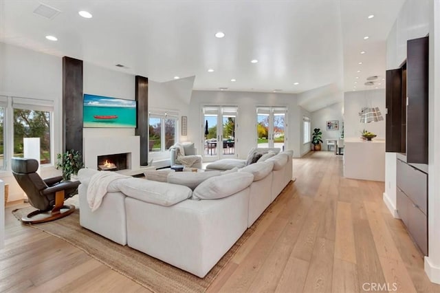 living room with a lit fireplace, light wood finished floors, visible vents, and recessed lighting