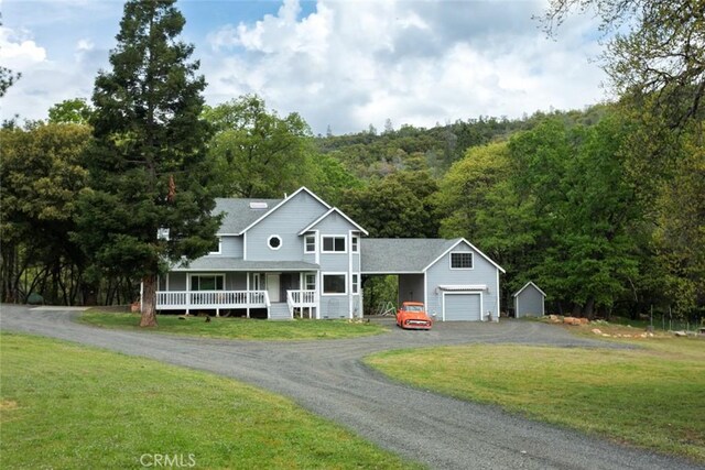 farmhouse inspired home featuring aphalt driveway, an attached garage, covered porch, a front yard, and a view of trees