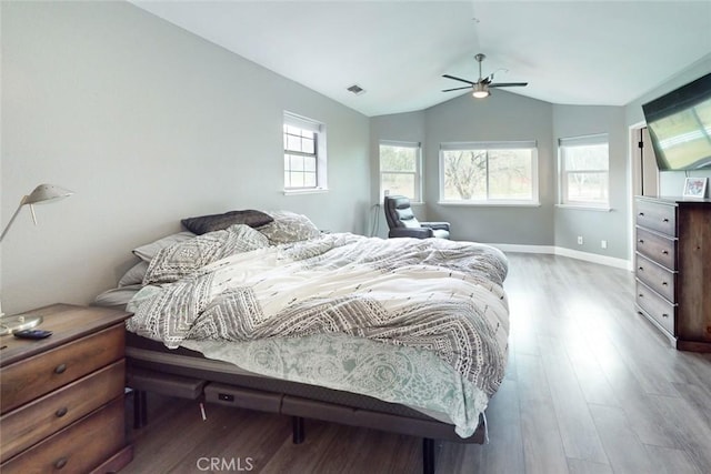 bedroom with multiple windows, vaulted ceiling, baseboards, and wood finished floors