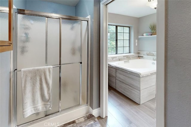 bathroom featuring a stall shower, a garden tub, a textured wall, and wood finished floors