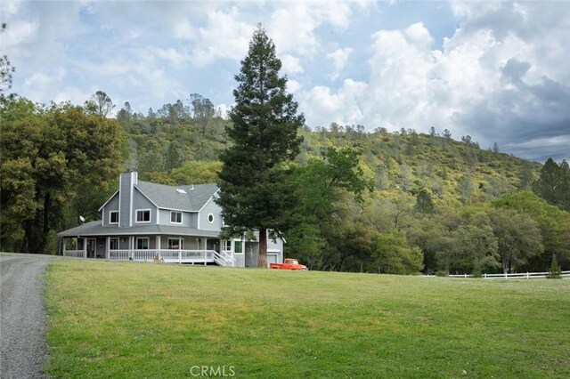 rear view of property featuring a yard, a chimney, a porch, a view of trees, and driveway