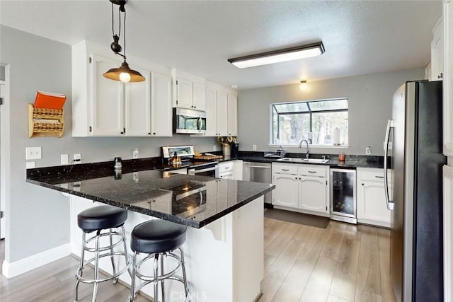 kitchen with wine cooler, appliances with stainless steel finishes, a peninsula, light wood-type flooring, and a sink