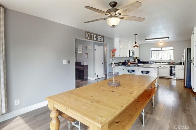 dining area with beverage cooler, wood finished floors, a ceiling fan, and baseboards