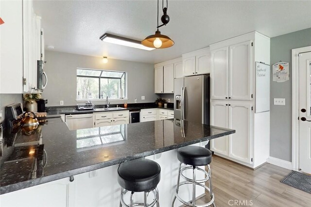 kitchen with a peninsula, a sink, white cabinetry, and stainless steel appliances