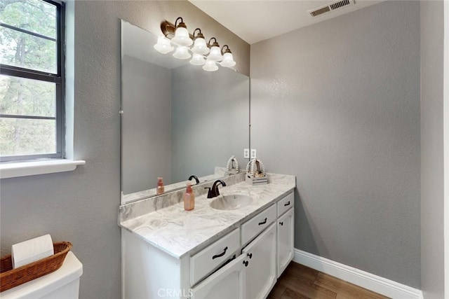 half bath featuring baseboards, visible vents, toilet, wood finished floors, and vanity