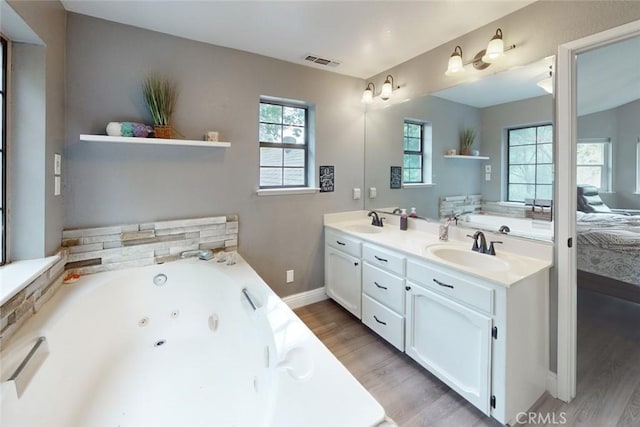 ensuite bathroom with visible vents, a sink, a whirlpool tub, and wood finished floors