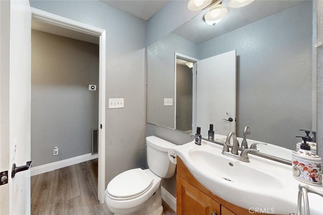 half bath featuring vanity, wood finished floors, toilet, and baseboards