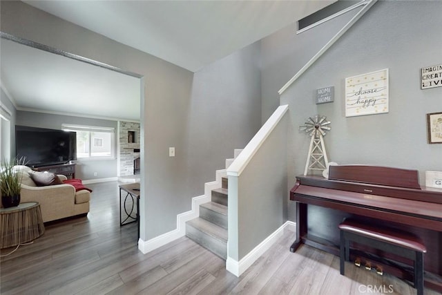 staircase with a large fireplace, baseboards, and wood finished floors