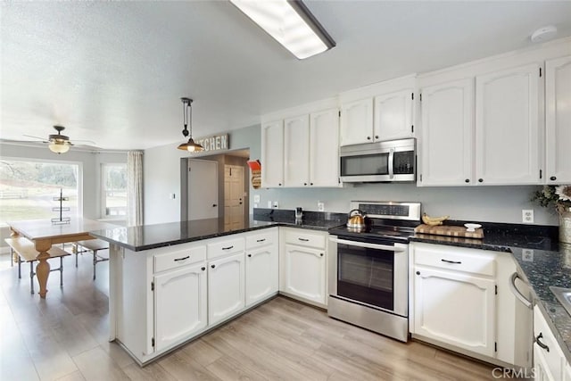 kitchen featuring a peninsula, light wood-style floors, white cabinets, appliances with stainless steel finishes, and decorative light fixtures