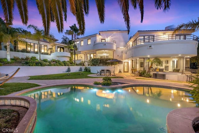 back of house featuring a fenced in pool, a patio area, a balcony, and stucco siding